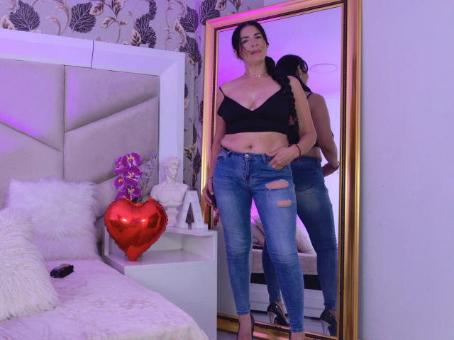 AlizonMoreti stands in front of a mirror, showing off her black crop top, blue ripped jeans, and black heels, with visible tits and a small ass. Reflection includes her back.