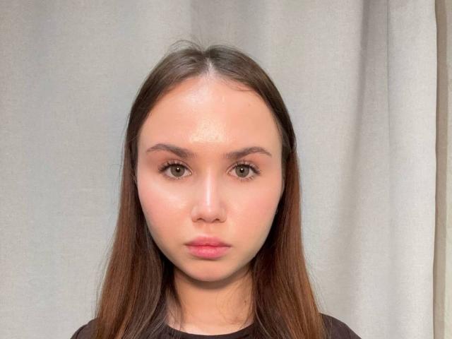 DenitaZahm tiene el cabello castaño lacio, ojos verdes y una frente brillante. Lleva una blusa negra y tiene una expresión neutra. Sus glúteos no son visibles..