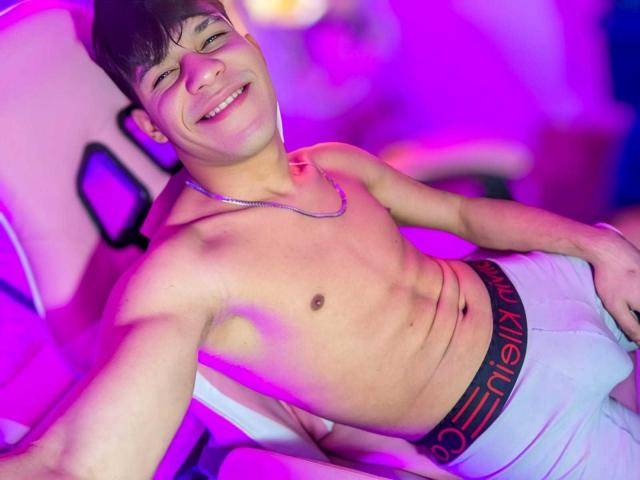 HottestKevin, shirtless, smiling, wearing white Calvin Klein underwear, silver necklace, lying back in chair, pink and purple lights, brown hair, cute, attractive, toned, relaxed, confident.