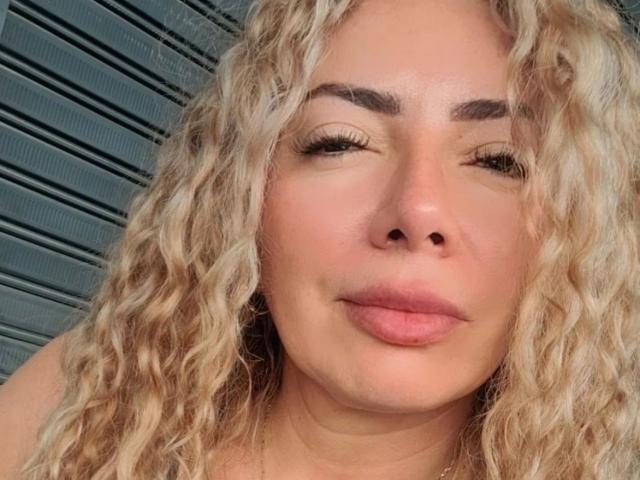 NaniDelaPavva hat lockiges, blondes Haar, volle Augenbrauen, geschlossene Augen und rosafarbene Lippen, die leicht zu einem Mund formt sind. Sie hat einen hellen Hautton und trägt keine sichtbare Kleidung..