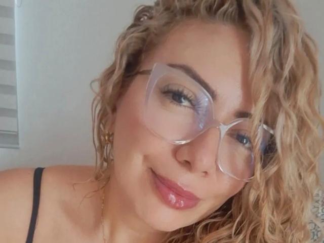NaniDelaPavva ha i capelli biondi ricci, porta occhiali dalla montatura chiara ed è sorridente, con il rossetto rosa. Indossa un top nero con spalline, che lascia intravedere leggermente il seno. Il suo viso è carino..