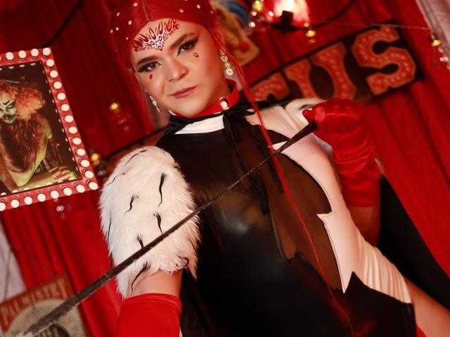 Shaina Monroe met een rode hoofdband, een zwart-wit outfit, rode handschoenen, die een zweep vasthoudt met een witte, pluizige punt, kijkend naar de camera, rode gordijnen, witte en rode lichten, een zelfverzekerde uitdrukking..