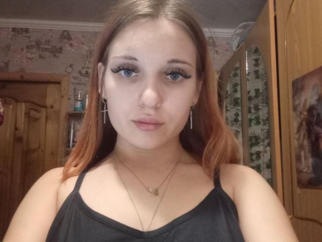 JanPasternack ha la pelle chiara, lunghi capelli rossi, occhi azzurri con un pesante trucco eyeliner, un piercing al naso e indossa una maglietta nera con spalline sottili, un seno piccolo e due collane..