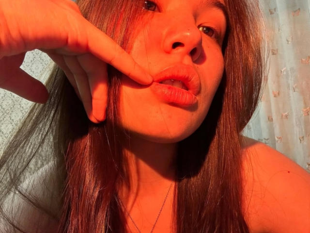 KaneshaNiederberger's face with long brown hair, red-orange lighting, and her index finger gently pulling her lower lip. She's looking slightly up with parted, glossy lips.