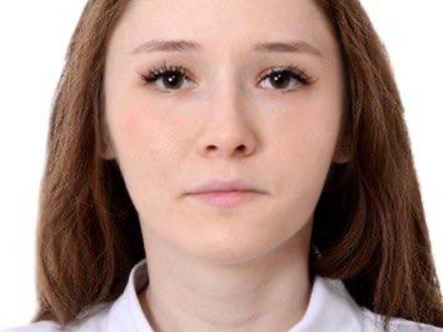 MarniePlantier has pale skin, brown eyes, and straight brown hair. She's wearing a white shirt, and her expression is neutral. Her small tits are slightly visible.