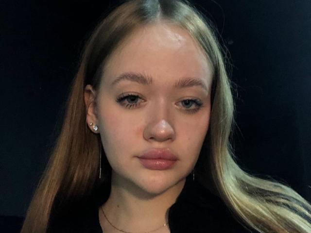 PamulaMetzner has light brown hair, pale skin, and small tits. She's wearing a black shirt, has subtle makeup, and is looking directly at the camera with a neutral expression.