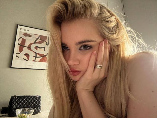 Nichelle Tetro, con cabello rubio largo, ojos azules y un anillo en la mano izquierda, apoyando su mejilla en la mano, mirando a la cámara con un ligero puchero..