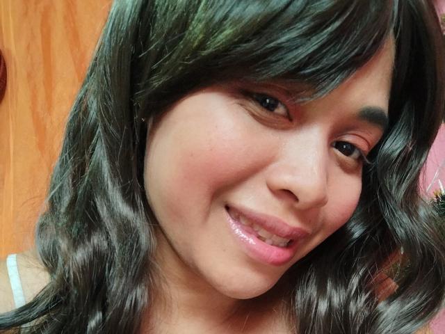 MithyMiss with shiny black wavy hair, pink glossy lips, and a slight smile, showing off her cute Asian face and dark eyebrows. Her nose is small and her skin is smooth.