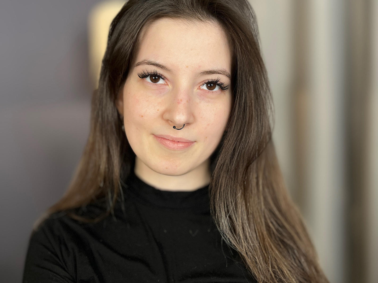 MariHouston with long brown hair, brown eyes, black eyeliner, nose ring, black turtleneck, slight smile, and fair skin, looking at camera.