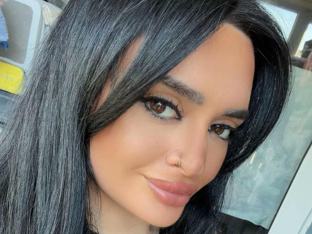 NightNymph heeft glanzend zwart haar, bruine ogen en een neusring. Ze glimlacht met lichtroze lippen en ziet er schattig uit. Haar wenkbrauwen zijn dik en ze draagt zwarte eyeliner..