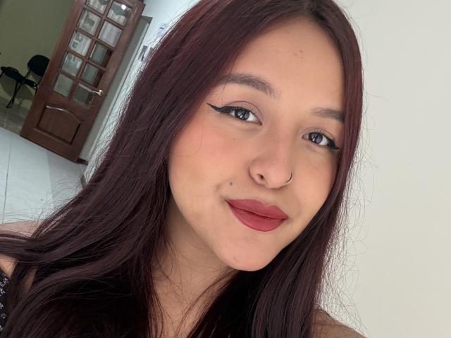 MarianaVargasX with long dark brown hair, nose ring, winged eyeliner, red lipstick, and a slight smile, showing her smooth, fair-skinned face. Boobs not visible.