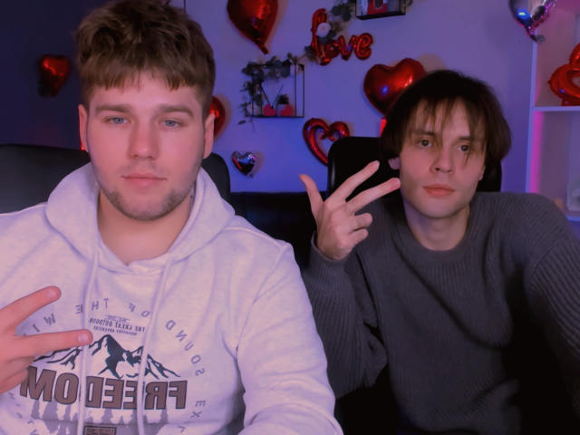 MichaelAlexCpl with a white hoodie and another MichaelAlexCpl with a gray sweater, both making peace signs, in a room with red heart balloons and blue lighting.
