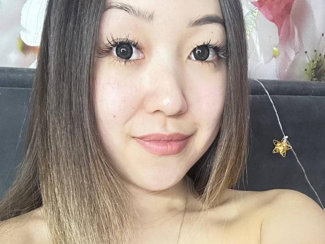RenyLime has long brown hair, big black eyes, and pink lipstick. She's topless with a small necklace featuring a gold star. Her boobs are not visible.