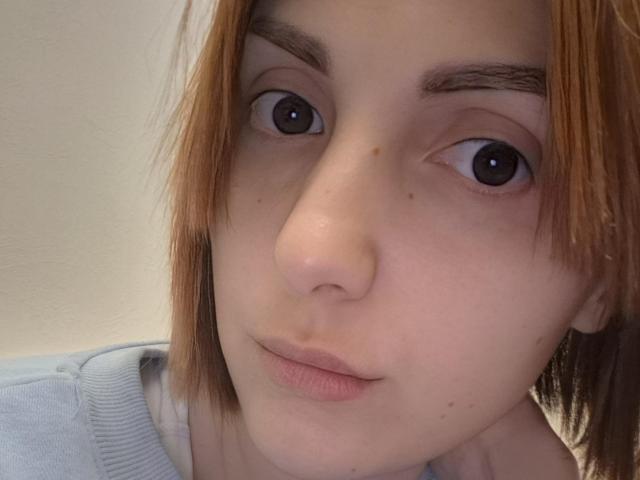 Het gezicht van EllaDestiny, met bleke huid, bruine wenkbrauwen en kort bruin haar, toont kleine borsten en een licht opgetrokken neus, met een neutrale uitdrukking en licht open lippen..