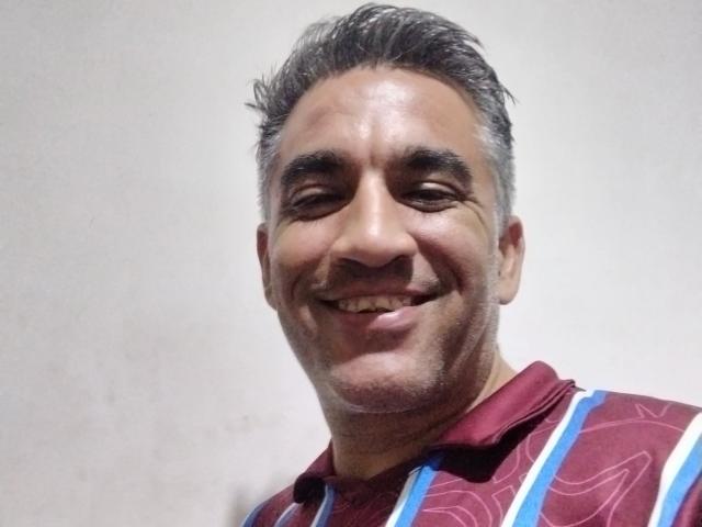 Joaoweb, un homme d'âge moyen, souriant avec des yeux marron, des cheveux gris, portant une chemise rayée rouge, bleue et blanche, avec une peau légèrement ridée et une expression joyeuse et détendue..