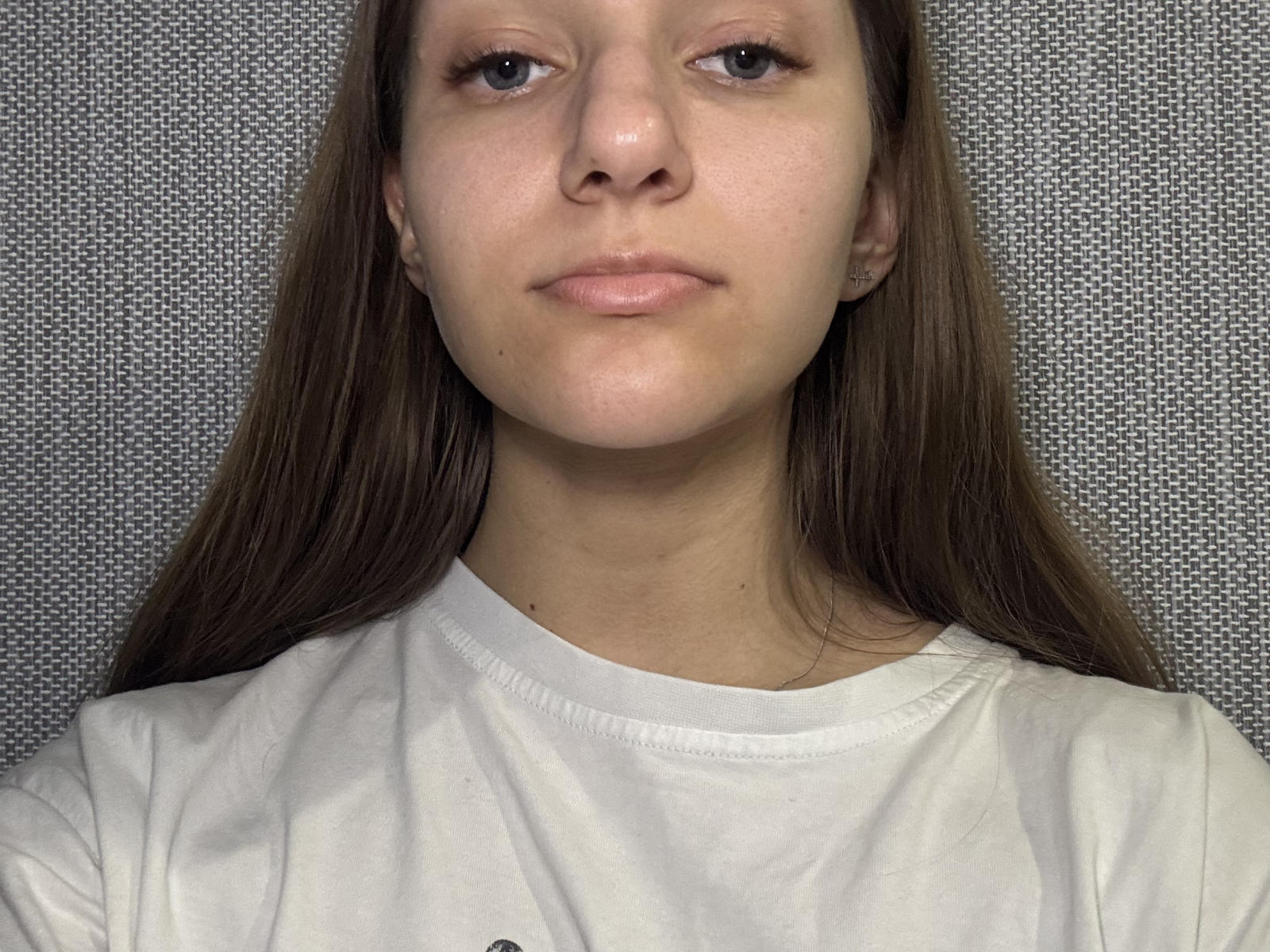 Lilith a les cheveux bruns lisses, une peau claire et de petites seins, elle porte une chemise blanche et a une expression neutre, sur une photographie..