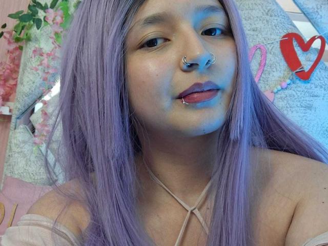 CandySwan with purple hair, nose ring, lip piercing, and blue face paint, sticking out tongue, wearing off-shoulder top, showing tits. Cute, punk, and slightly messy look.