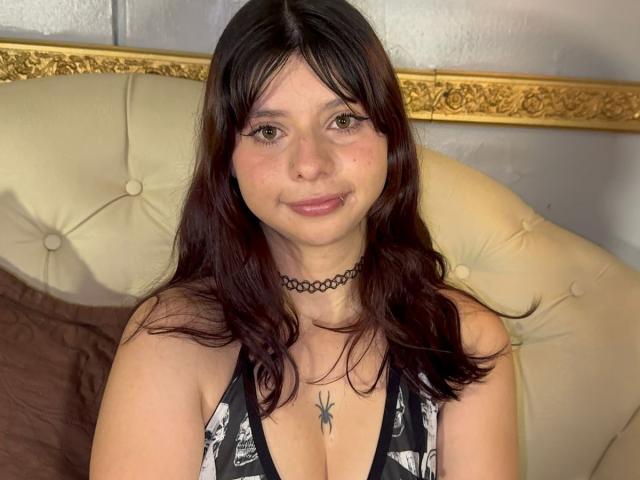 SofiWalton has brown hair, a black choker, and a spider tattoo between her tits. She's smiling with subtle makeup, wearing a black and white patterned top.
