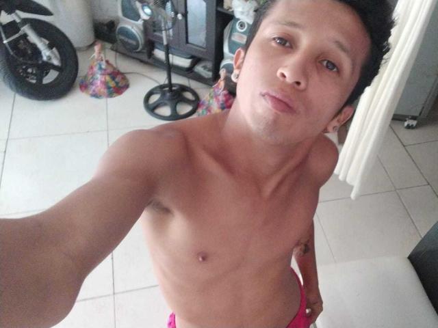 NickHotX, sin camisa, con un cuerpo delgado y tonificado, pezones pequeños y una ligera expresión de puchero, lleva ropa interior rosa, tiene el pelo corto y negro y una expresión neutra, y está tomando un selfie..