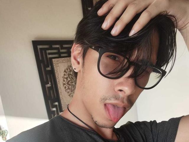 KingDanny, con gafas negras, sacando la lengua, con una mano en el pelo, vistiendo una camisa negra y un collar, tiene un ligero bigote y barba, y piel clara, en un selfie..