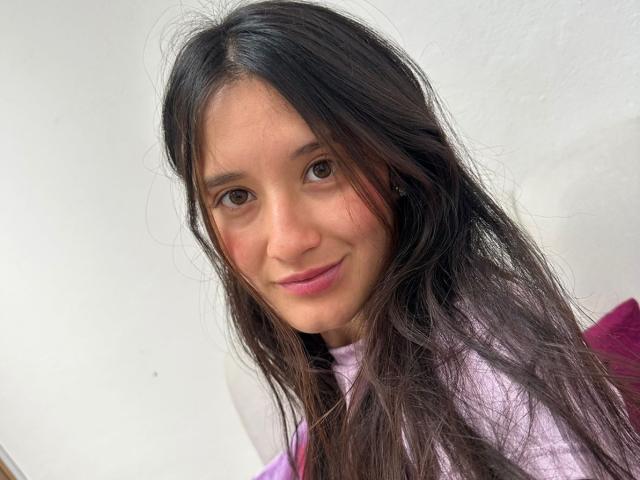 KimyRosse has long, messy black hair, brown eyes, pink lipstick, and a slight smile. She's wearing a pink and purple top, with a white background.