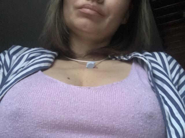 ElizavetaCream's face, showing her puffy pink ribbed tank top, striped blue and white jacket, and white necklace, with her small tits and brown hair visible.