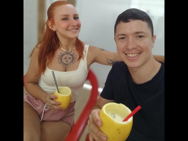 RuivaK with red hair, white tank top, and pink shorts, holding a yellow coconut with a straw, sits next to RuivaK with short black hair, black shirt, and matching coconut.