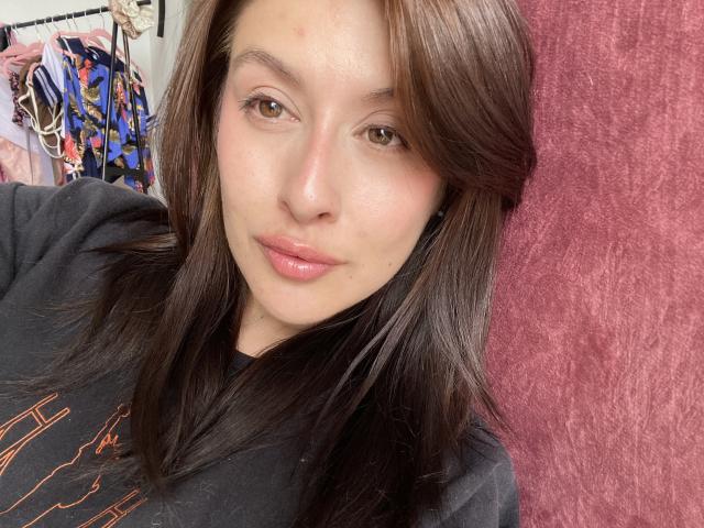 IsabellaPalacio has shiny brown hair, light skin, brown eyes, and glossy pink lips. She's wearing a black shirt and looking at the camera with a subtle smile.