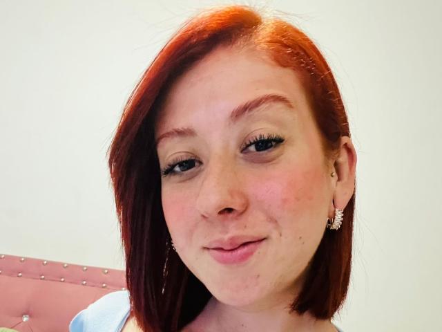 Valeriaaf has red hair, light skin, and a slight smile with pink lips. She's wearing small earrings and has long, dark eyelashes. Her face shows a few freckles.