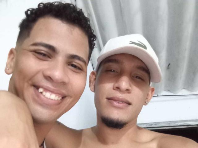 MaikolAndAndry with curly black hair and MaikolAndAndry with a white cap, both smiling, shirtless, showing their bare shoulders, and a small black mustache.