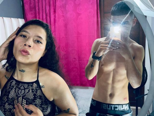 DuoPerverCrazy, avec ses cheveux noirs bouclés et ses tatouages, porte un haut en dentelle et fait une moue. DuoPerverCrazy, torse nu avec un corps mince et musclé, prend un selfie devant un miroir, le flash obscurcissant son visage..