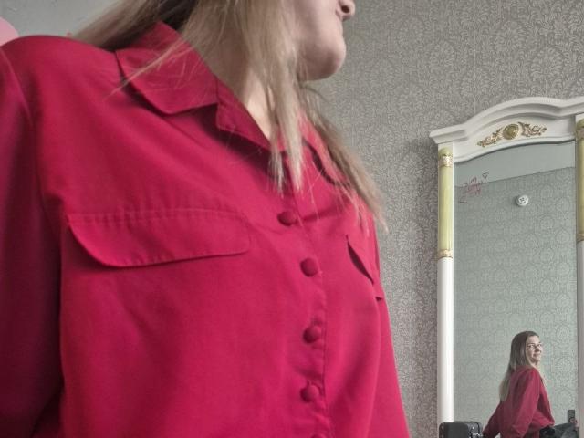 Anshante's red shirt with buttons and pockets, showing her upper body and blonde hair, reflected in a mirror. Her face is partially visible in profile.
