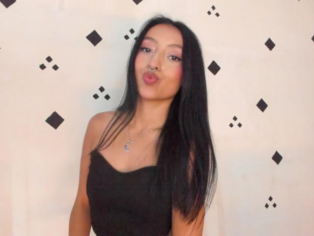 HotMoonX with long black hair, nose ring, pouty pink lips, wearing a black strapless top, and a silver necklace, looking directly at the camera.