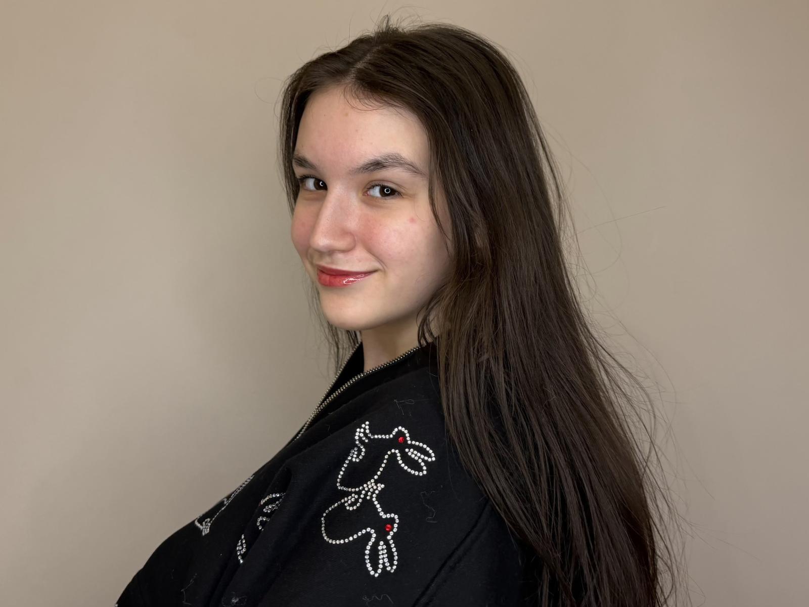 MarleneLown with long brown hair, black embroidered shirt, slight smile, and red lipstick, facing camera, showing her back, cute, and looking over her shoulder.