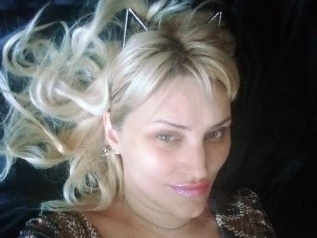 FreyaMillyy with blonde, wavy hair, wearing metal cat ears, and a shiny necklace, has a slight smile, showing her pink lips, and is looking at the camera.