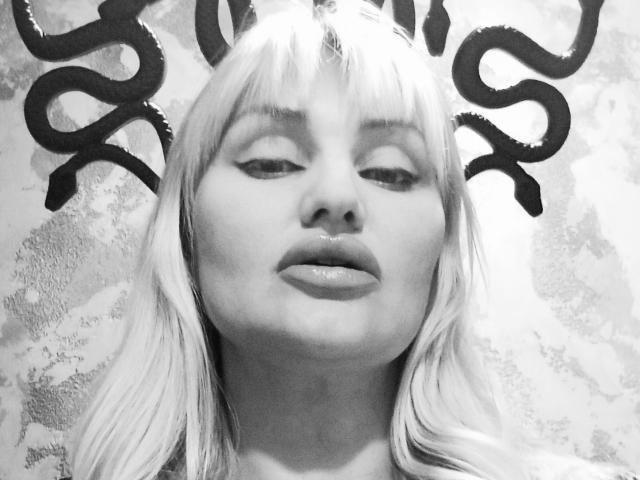 FreyaMillyy, con i capelli biondo platino, labbra piene e la bocca leggermente aperta, guarda verso l'alto dei vortici di graffiti neri in una fotografia in scala di grigi..