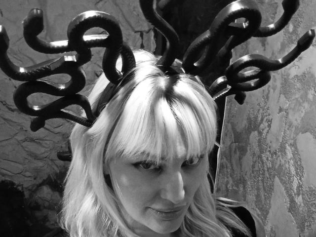 FreyaMillyy con una brillante pieza para el cabello negra, similar a un tentáculo, cabello blanco-rubio y una sutil sonrisa, en una fotografía en blanco y negro. Su trasero no es visible, solo su rostro..