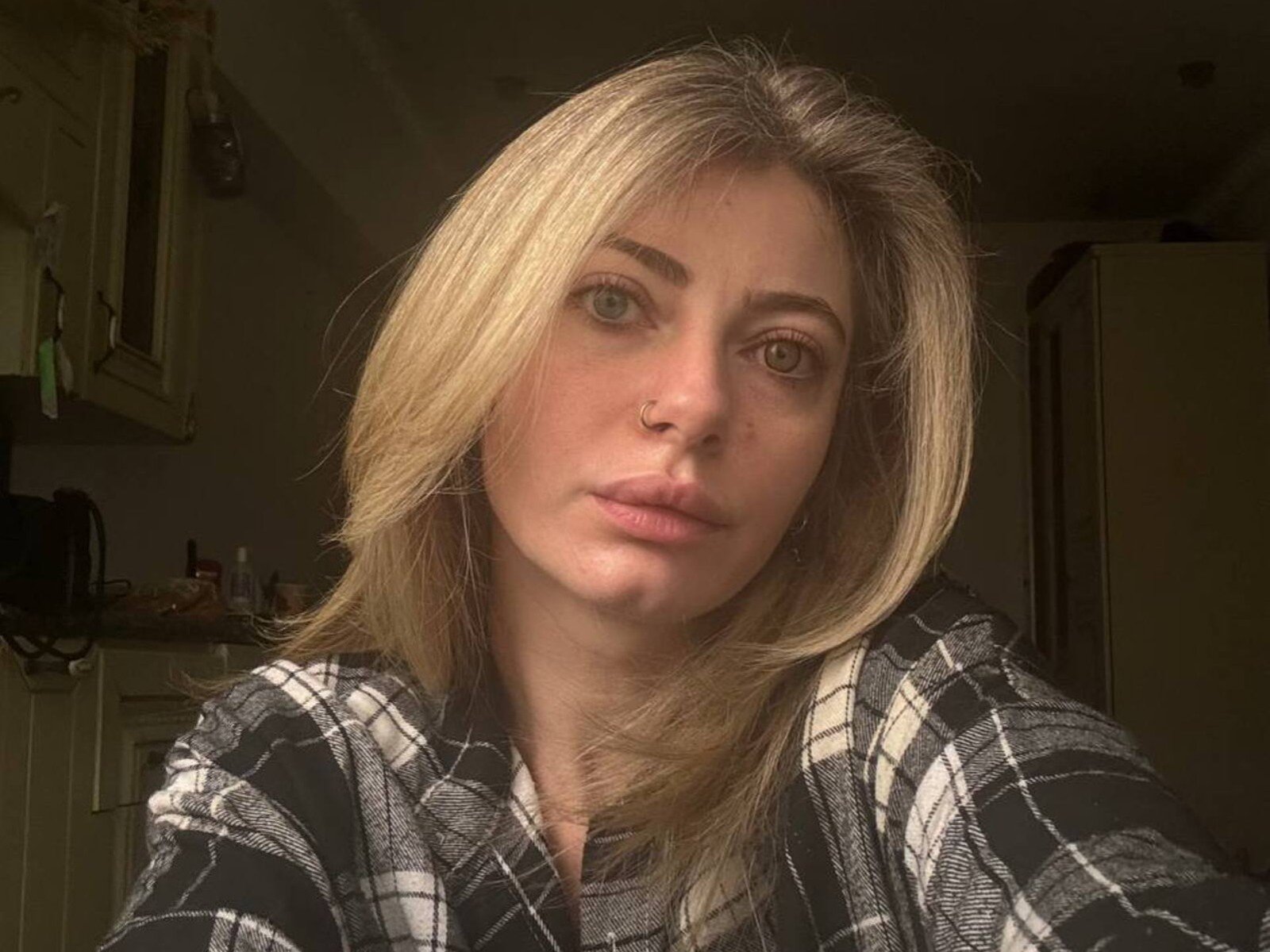 Dania Barsegyan, mit blonden Haaren, grünen Augen und einem Nasenring, trägt eine schwarz-weiße Karohemd und blickt mit einem neutralen Ausdruck in die Kamera..
