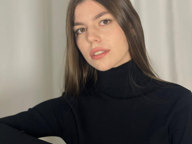 Photograph of StacyStripling, a fair-skinned woman with long brown hair, wearing a black turtleneck, arms crossed, brown eyes, slightly parted pink lips, soft natural light, slight shadow on face.