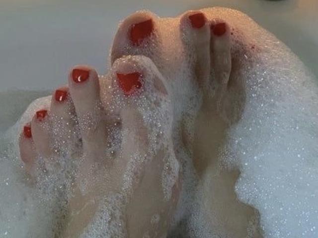 Close-up dos pés de SarahFontain, com unhas dos pés pintadas de vermelho, cobertos de bolhas de sabão, mostrando uma imagem provocante e sensual. vibração. Pele macia e úmida, dedos ligeiramente afastados, criando uma atmosfera sensual e íntima..