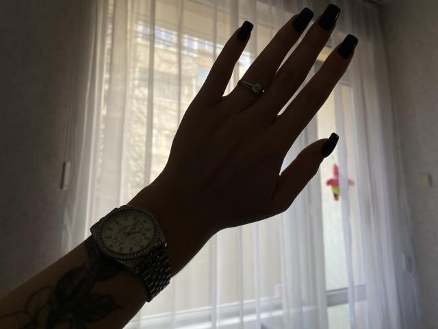 De silhouet van de hand van Olieri, met de palm naar boven gericht en de vingers gespreid, draagt een horloge met een gedetailleerde wijzerplaat en ringen aan alle vingers. vingers. Scherpe, zwarte nagels, met achtergrondverlichting van een helder raam..