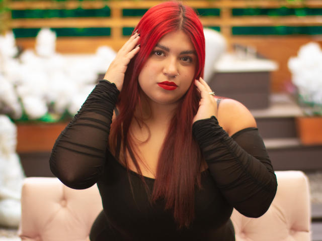 AmberCutel, com longos e vibrantes cabelos ruivos, vestindo uma blusa preta com um ombro descoberto, tocando o cabelo com as duas mãos, totalmente ruiva. lábios, olhar intenso, fundo brilhante e desfocado, pose sexy e confiante..