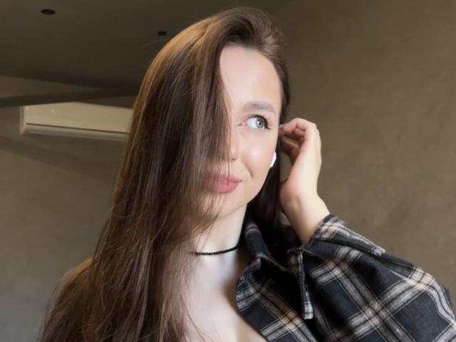 Photograph of Murris, a young woman with long brown hair, blue eyes, and red lips, wearing a black plaid shirt, touching her hair with a sexy, suggestive look, soft light.