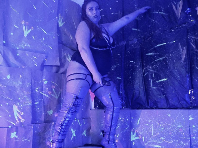 LexyDom está de pie en una habitación oscura, vestida con un conjunto de lencería negra con tirantes y botas hasta el muslo. Ella se estira, iluminada por una luz de neón azul, con mariposas brillantes a su alrededor. Increíblemente atractivo/a..