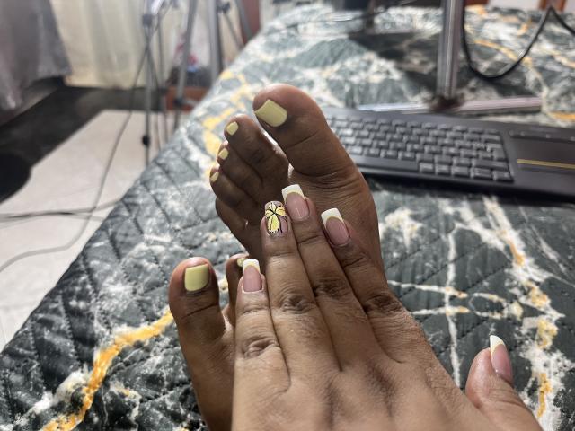 Close-up of MelanyScoth's feet on a black marble surface with white and orange veins. MelanyScoth's toenails are painted yellow, pink, and adorned with a small gold design. Laptop in background.