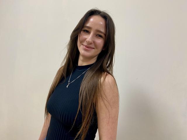 Omella stands with a slight tilt, long brown hair wet and slicked back, wearing a tight black sleeveless top, smiling. She has a scar on her right arm. Fucking sexy.