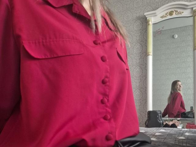 Close-up van Anshante in een rood overhemd met knopen, met de nadruk op de borst en schouders, vage achtergrond met een andere Anshante. zittend in de buurt van een spiegel, gekleed in het rood, in de buurt van speakers en een tafel.