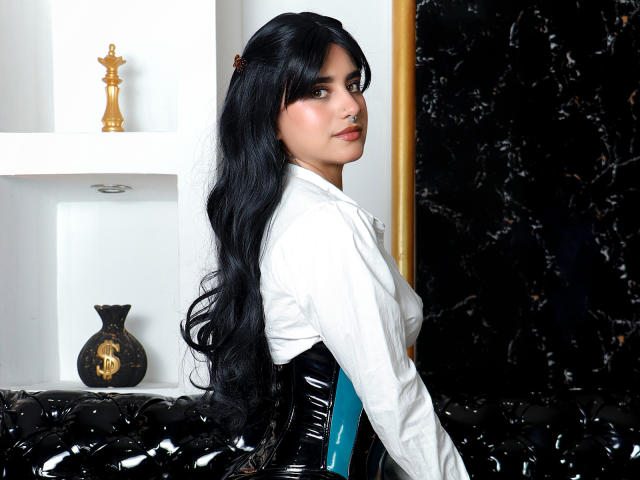 SamanthaGio, una mujer atractiva con cabello largo y negro, lleva una camisa blanca, ligeramente girada para mostrar su perfil. Labios rojos.
fondo en blanco y negro, estatua dorada, jarra negra..