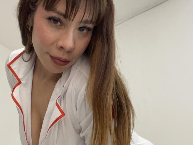 Close-up de AriiannaHot, uma mulher asiática com cabelos castanhos longos, vestindo uma camisa branca com detalhes vermelhos, decote baixo que revela decote, sorriso discreto, piercing no nariz, olhando para a câmera, tensão sexual, olhar sedutor..