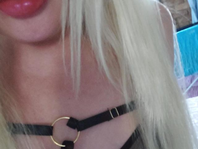 Nahaufnahme des Gesichts und der Brust von YourCoronet, die platinblondes Haar, roten Lippenstift und ein schwarzes Lederarmband zeigt. Goldener Ring.
haare verdecken teilweise einen Hauch von Ausschnitt. Sexuelle Spannung..